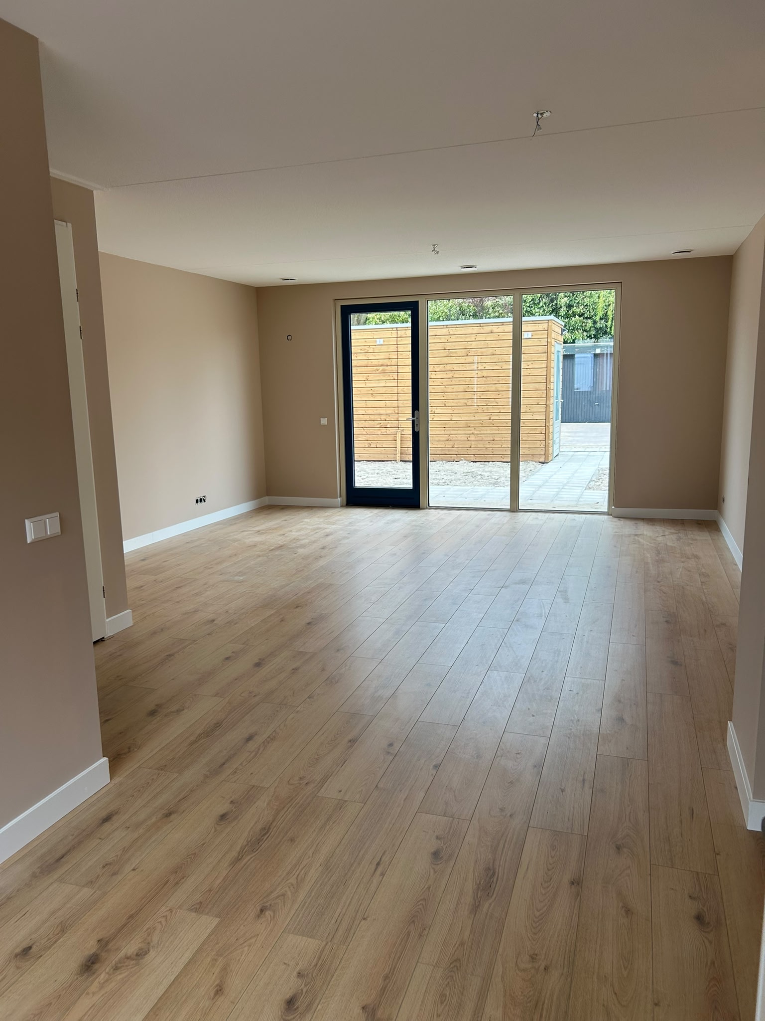 Woonkamer met warme neutrale wandkleur en lichte vloer