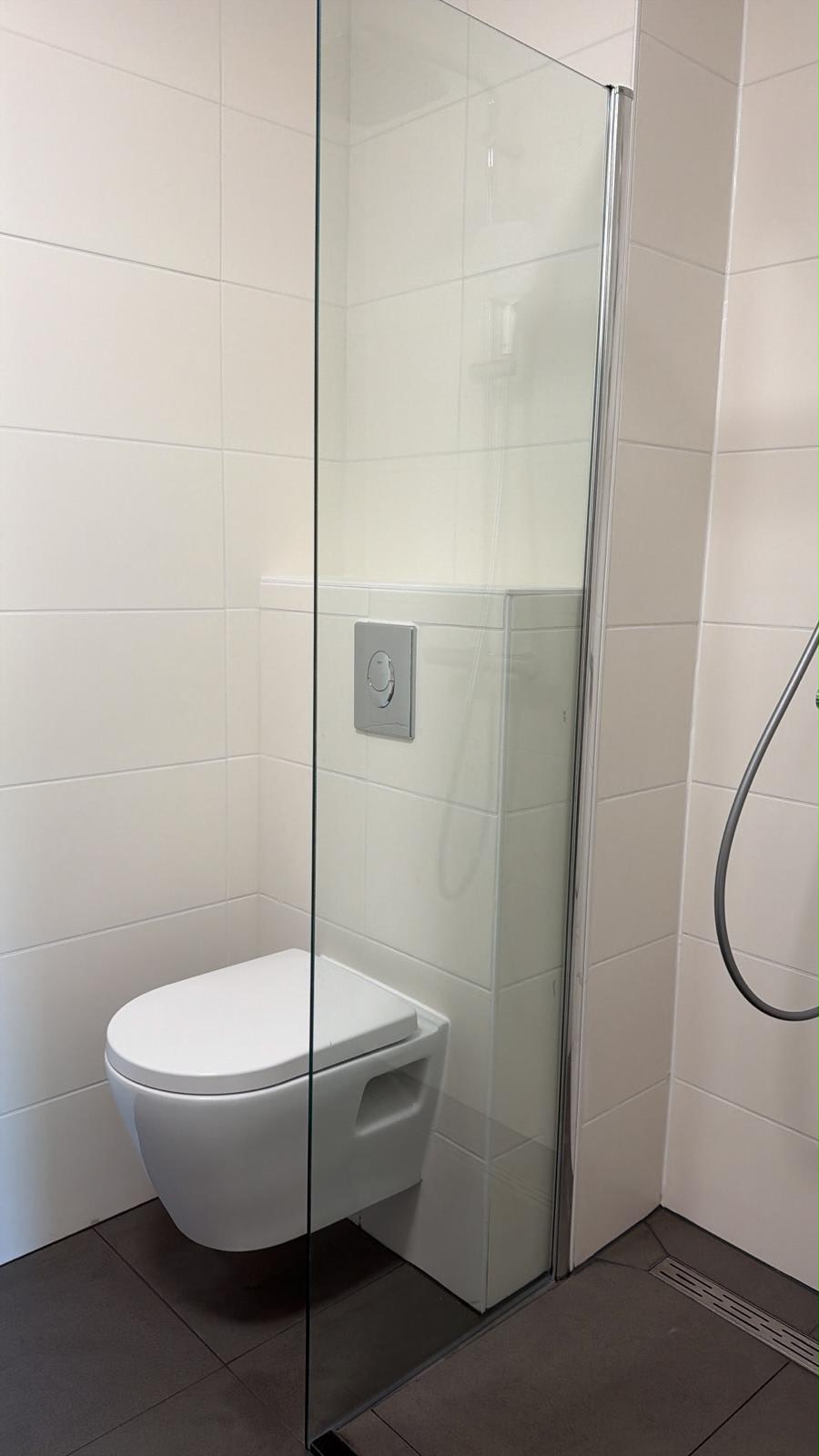 Toilet en glazen douchewand in compacte badkamer